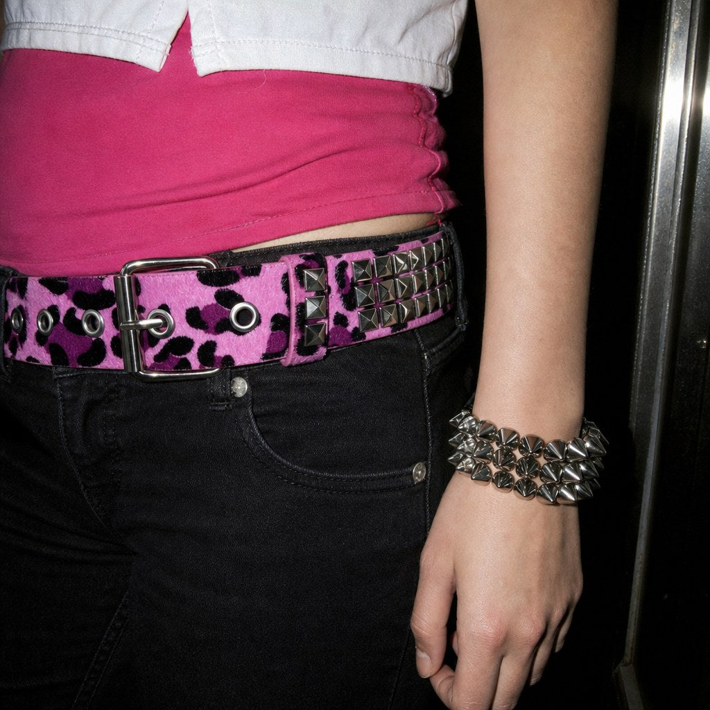 Close view of a pink leopard-print studded belt on black jeans with a silver spike bracelet